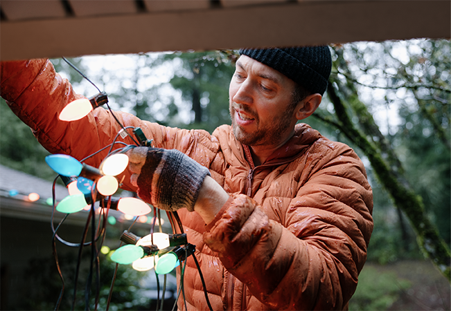 A man hanging colorful Christmas lights on his home